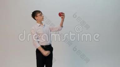 一个学生或一个带着眼镜和一件白色衬衫的小学生把拳头和一个红苹果相比。 一个长相滑稽的少年表现出不同的